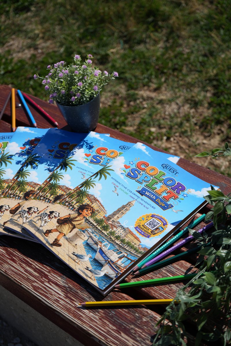 Several copies of Color Split with Duje fanned out on a wooden bench beside coloured pencils and a small flowering plant.